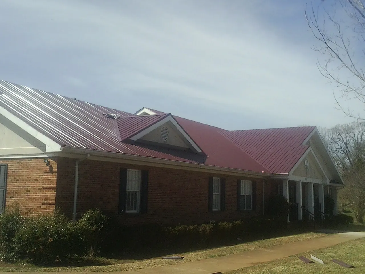 Red metal roof with gabled entries on a long brick building, from a Hail Damage Roof Repair job in Curwensville