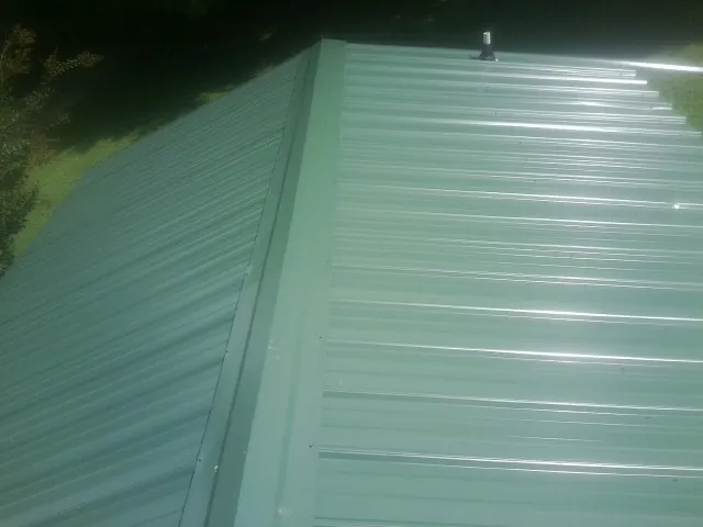 New green metal panels meeting at the ridge of a roof — Flat Roof Repair work by our crew in Curwensville