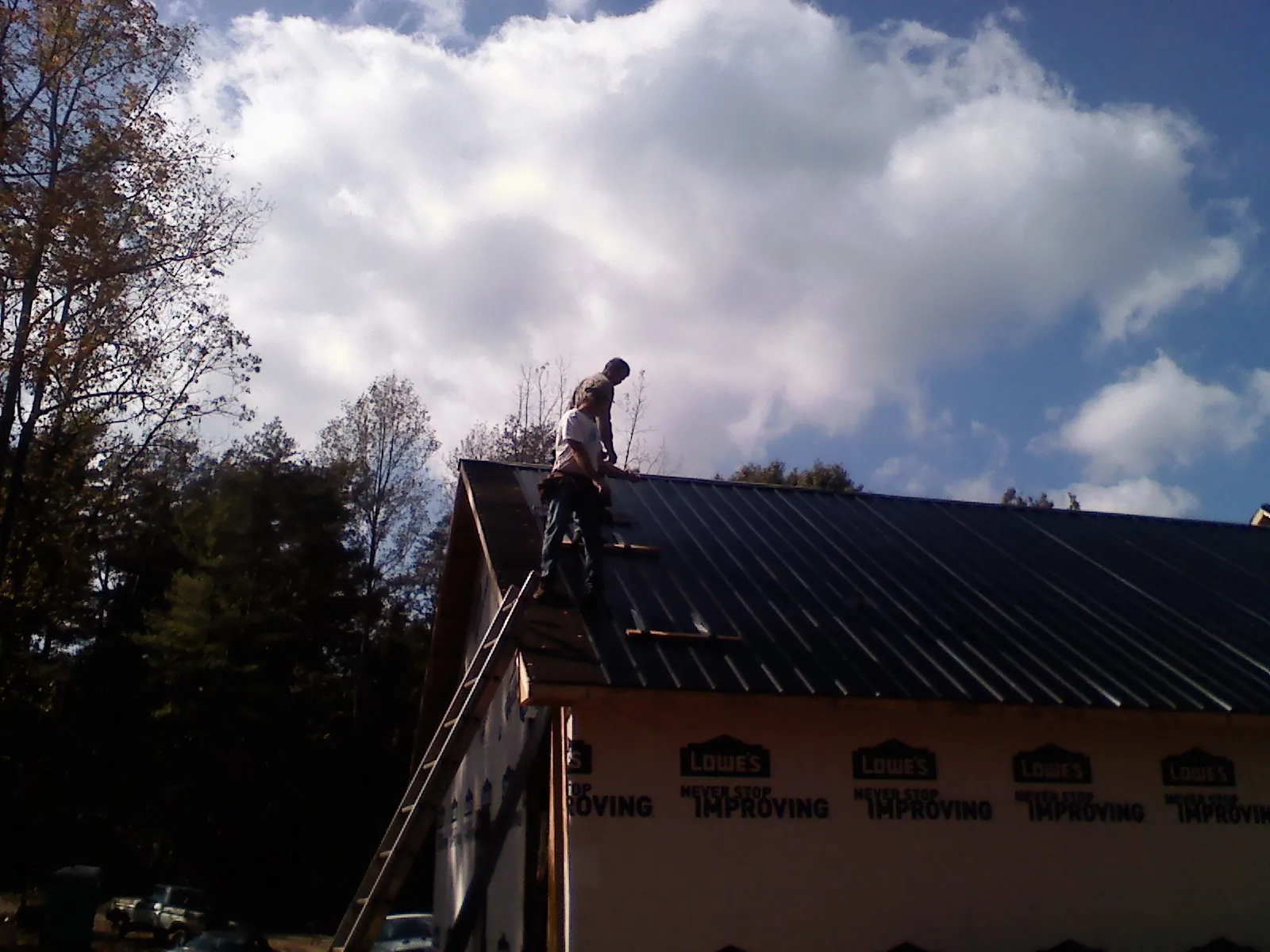 Roofer fastening dark metal panels high against a cloudy sky, from a Roof Inspection job in Curwensville