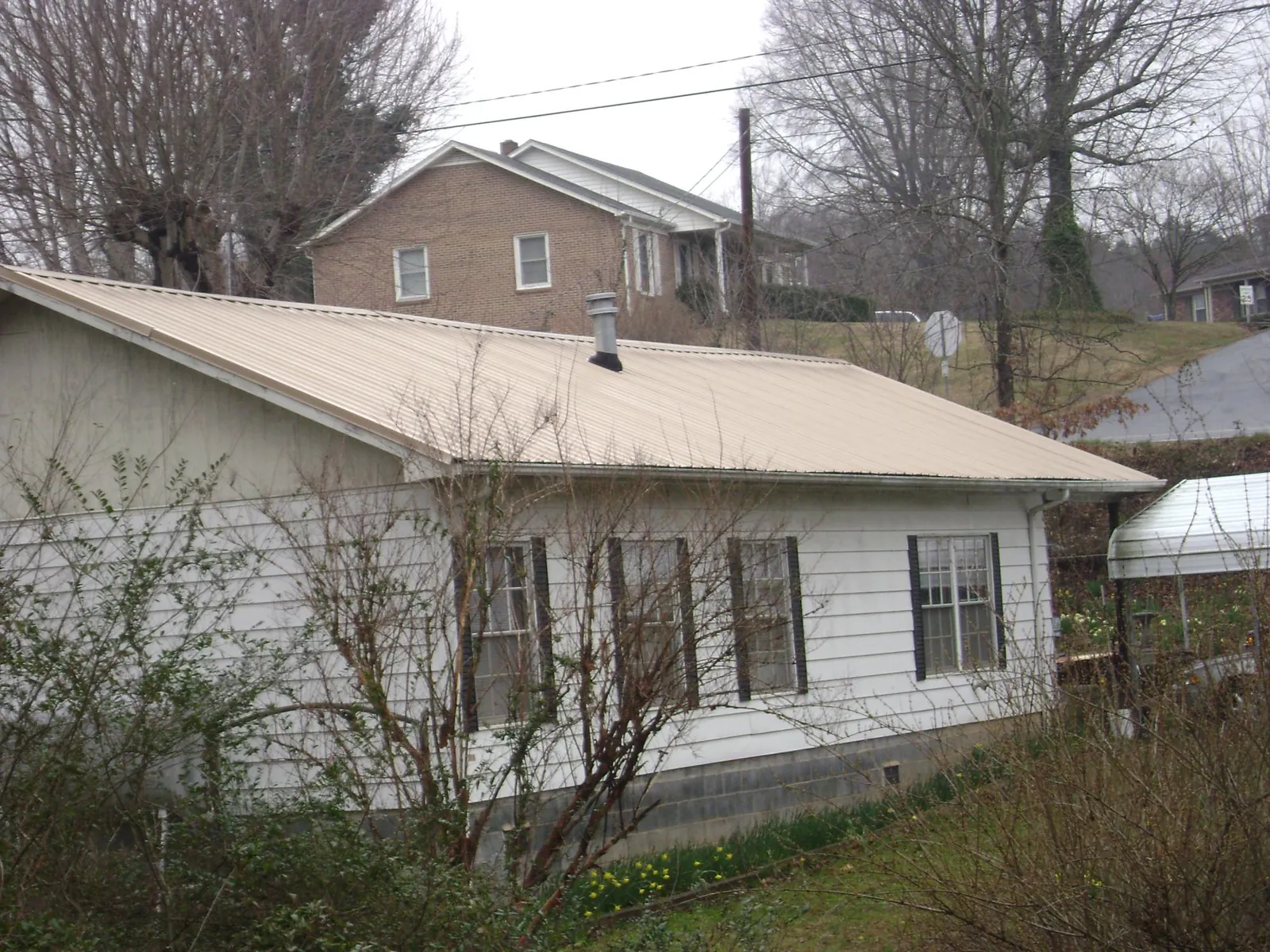 Tan metal roof on a white sided house set into a hillside — Commercial Roofing by Roofing Brothers in Curwensville